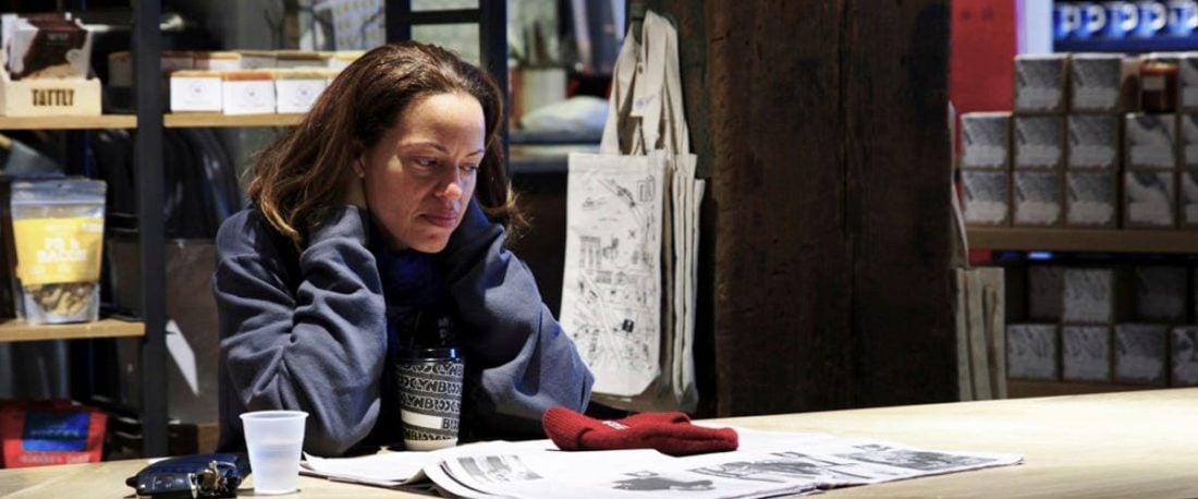 Still from "On the Record" movie. A woman sits at a table and looks at an open newspaper.