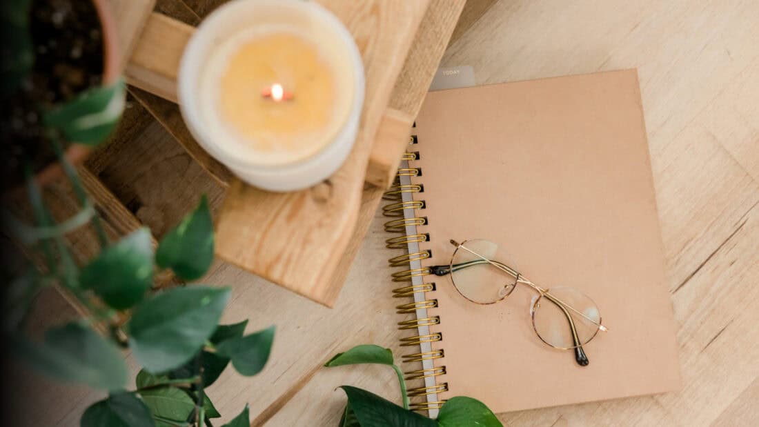 Desk with journal, eyeglasses, plant, and candle