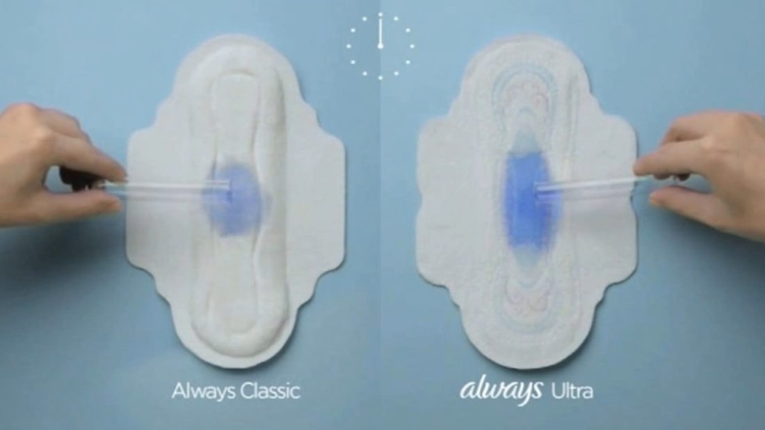 Two hands hold identical droppers depositing blue liquid onto two sanitary pads on a light blue background. The left pad is labeled "Always Classic," and the right pad is labeled "Always Ultra," showing product absorption comparison without any TMI details.